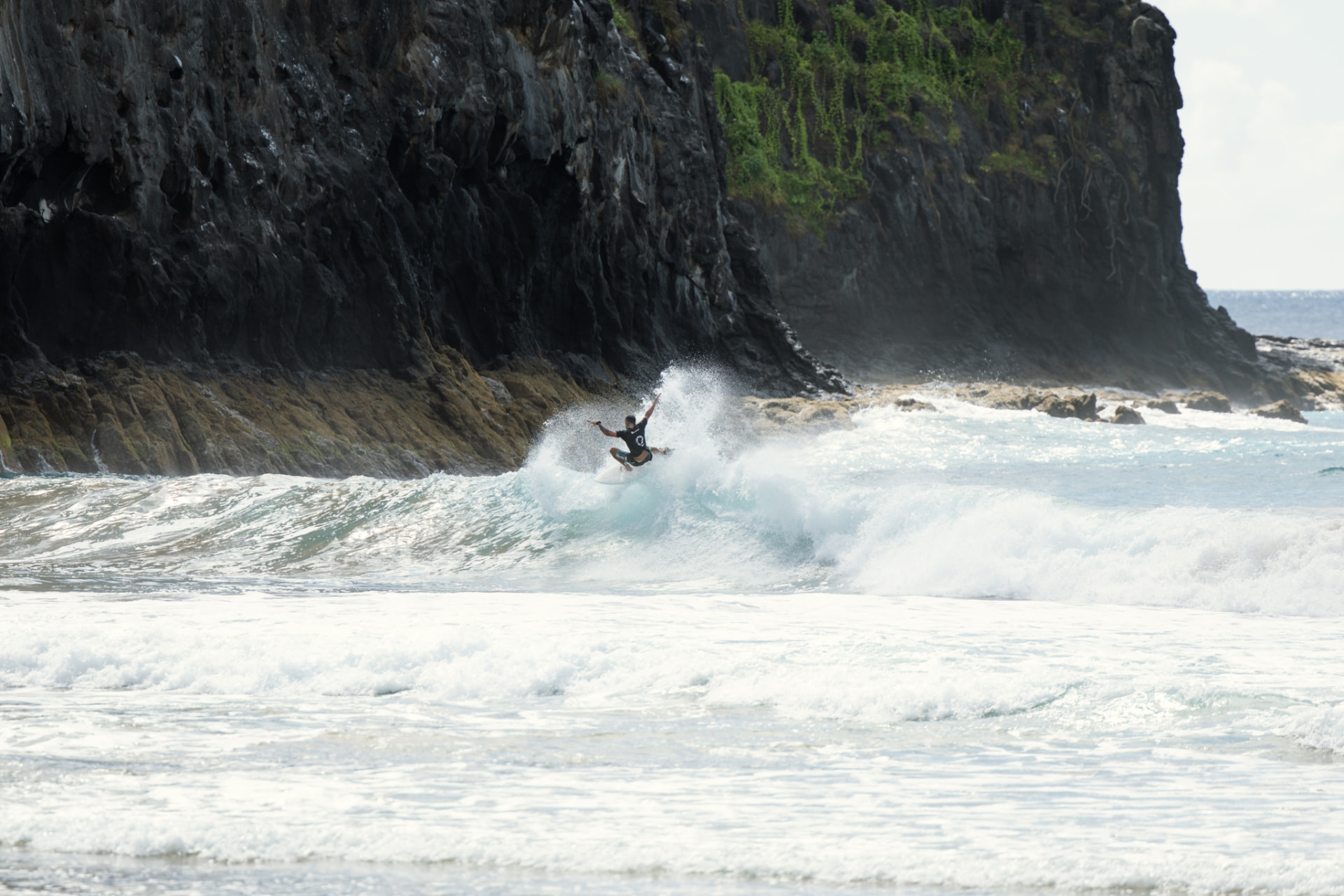 Surfista em manobra em uma onda diante das falésias de Fernando de Noronha